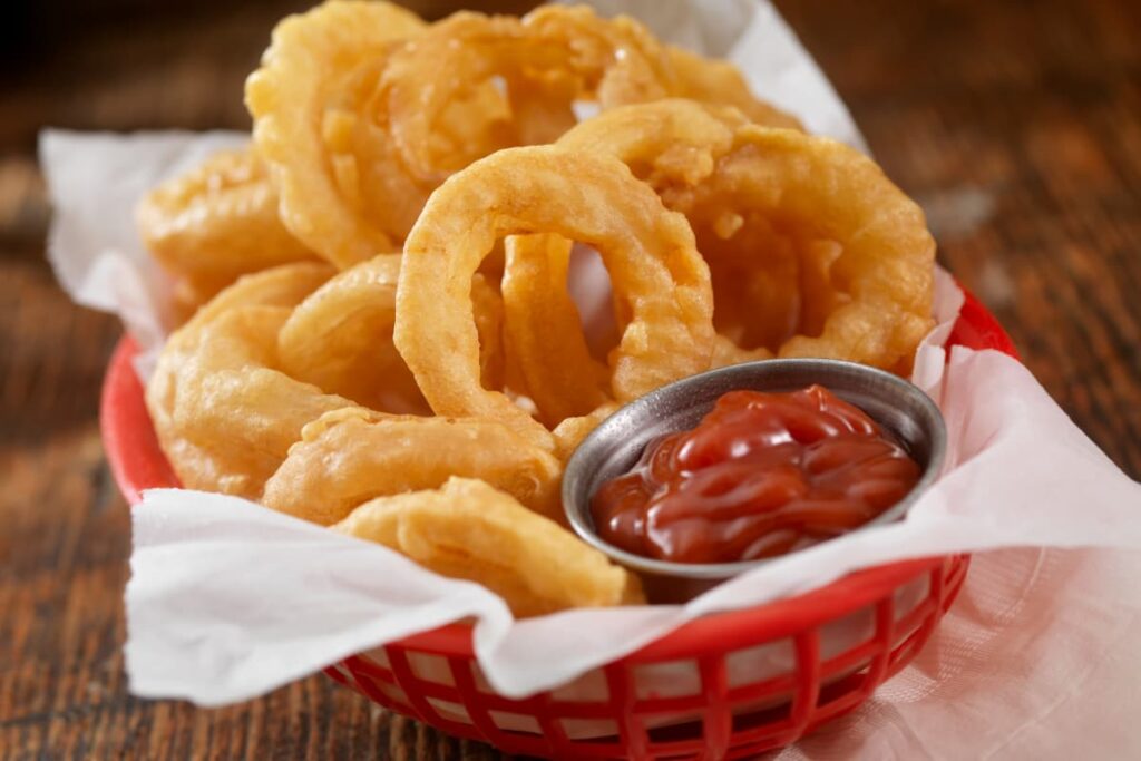 Burger King Onion Rings are served in a red bowl which has white tissues and red ketchup in a small steel bowl.