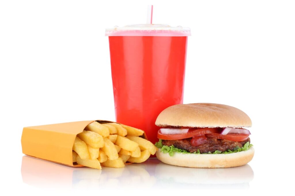 Wendy's Happy Meals has a burger with a Pattie, few slices of tomatoes, onion and lettuce, a drink in red colour cup with a straw in it and bunch of French fries in yellow packet.