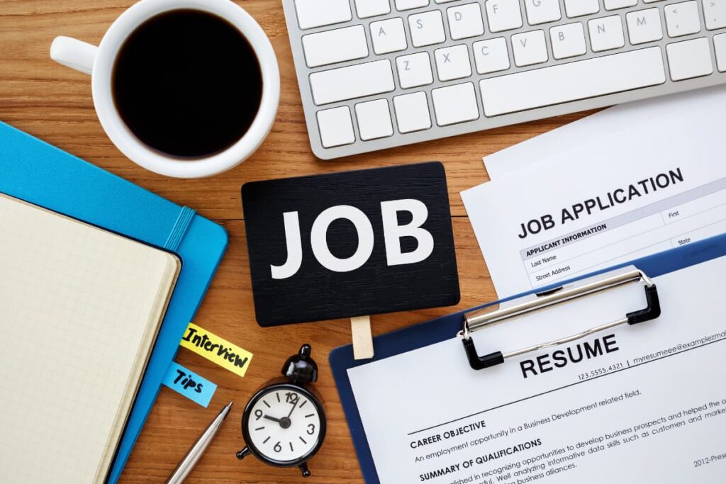 Applying Job at Walmart on a table consists of job application, Resume,  one laptop, one black color alaram, one pen and a mug with a black coffee.