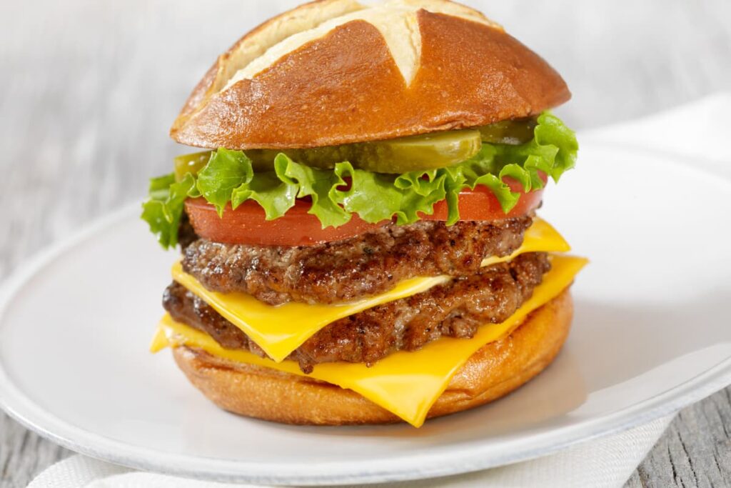 Burger King Double Cheeseburger serves in a white plate, this burger includes 2 beef patties, 2 cheese slices, along with tomato slices, and lettuce.