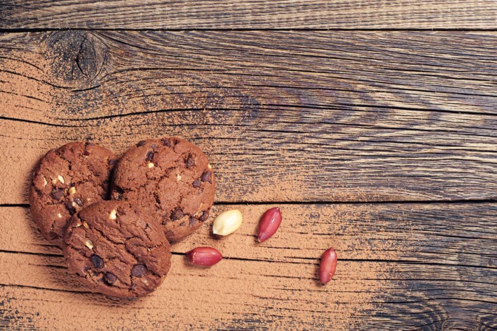 Chick Fil A Cookies Have Nuts on top. There are 3 brown almond cookies which are placed on the table, beside cookies some almonds are placed.
