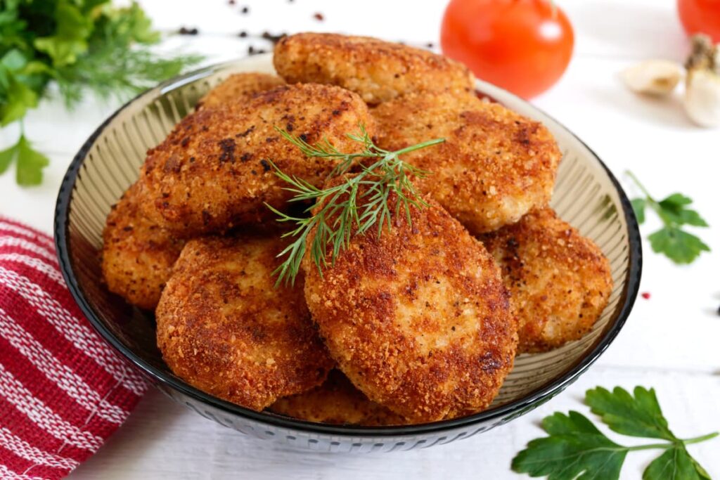 Chick Fil Spicy Nuggets are served in a glass bowl, and it is garnished with the Dill. Besides of the Spicy chicken nuggets there is a red towel, coriander leaves, garlic and tomato.