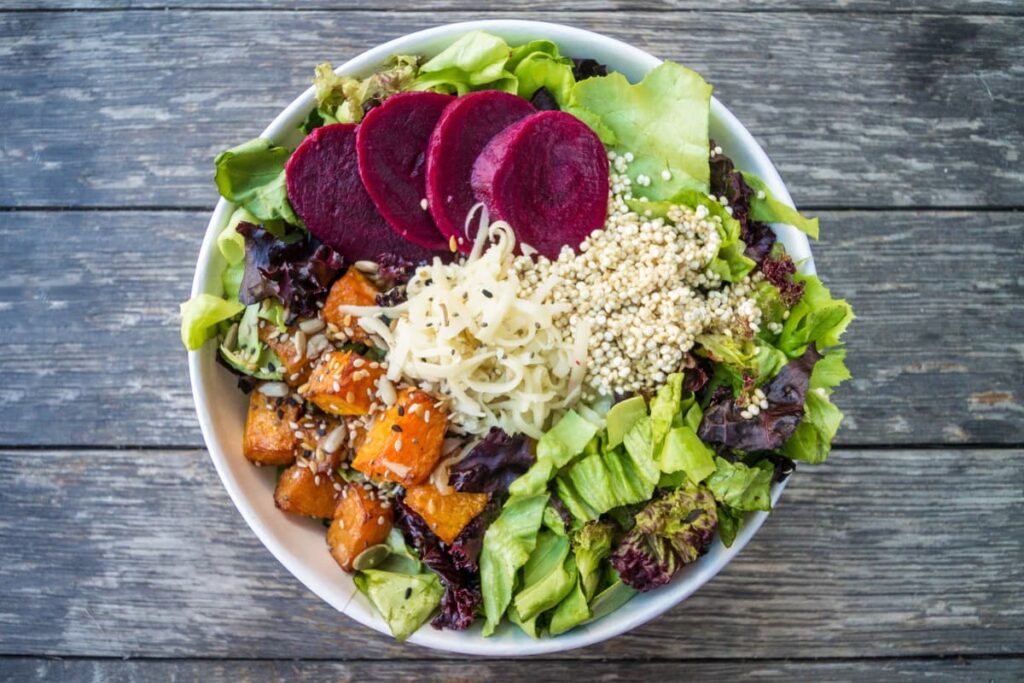 Chick Fil A Vegan dishes are served in a white bowl. It is a mixture of leafy vegetables, lettuce, beetroot, carrot, sesame seeds, Quinoa rice, sliced onion.