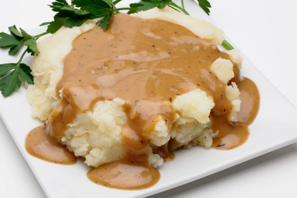 Chick-Fil-A Serves Gravy on a mashed potatoes, which is on the white saucer. Chick Fil A serves gravy which is brown in color and it is garnished with coriander leaves.