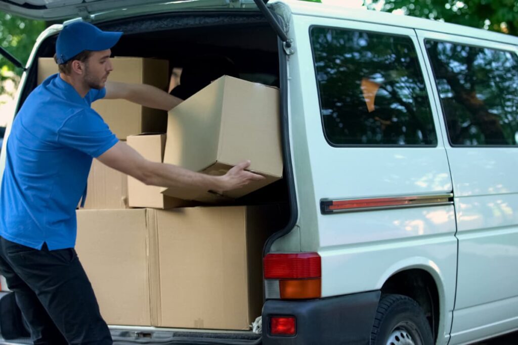Lowe's appliance delivery package carried by a delivery boy with blue shirt and cap picking the bulk of boxes from a white van.