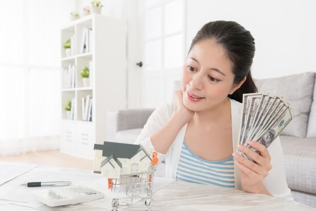 Walmart Cash Savings Bonds applied by a women with holding eight dollars sitting in front of her desk consists of pen, calculator, piggy bank and a mini cart.