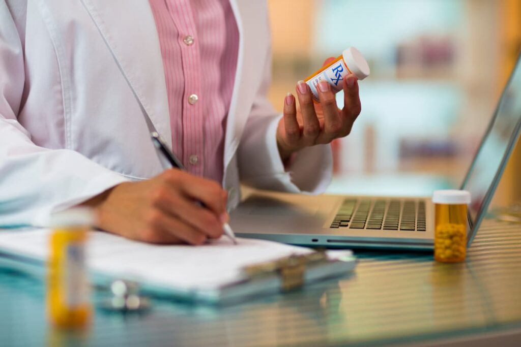 A Walmart Pharmacist write down the prescriptions in laptop and note down on a book with pen along with some medicines through Walmart prescriptions delivery service.