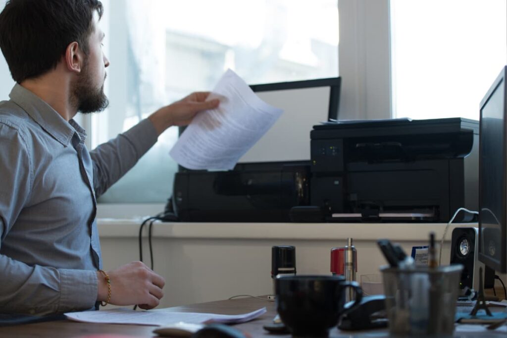 A man printing documents with the help of printer at Walmart and also appearing one cup, Desktop and a pen holder on his desk.