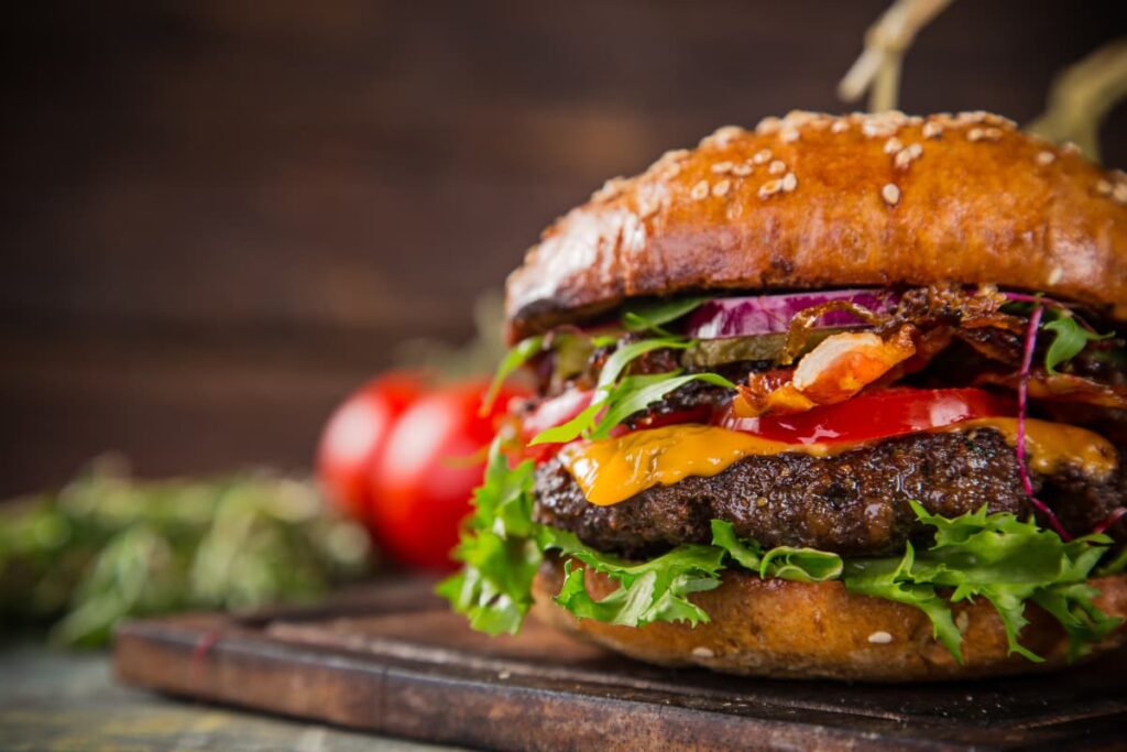 Burger King Burger serves in a brown color wooden plate. This burger contains beef patties, mayo sause, onion slices, tomato slices, jalapeno and lettuce.