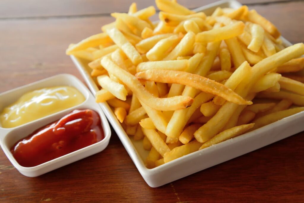 Burger King Fries can be served in a white plate which is placed in a brown color table. Along with french fries also served red color ketchup in a small white color cup and mayonnaise in a small white color cup. 