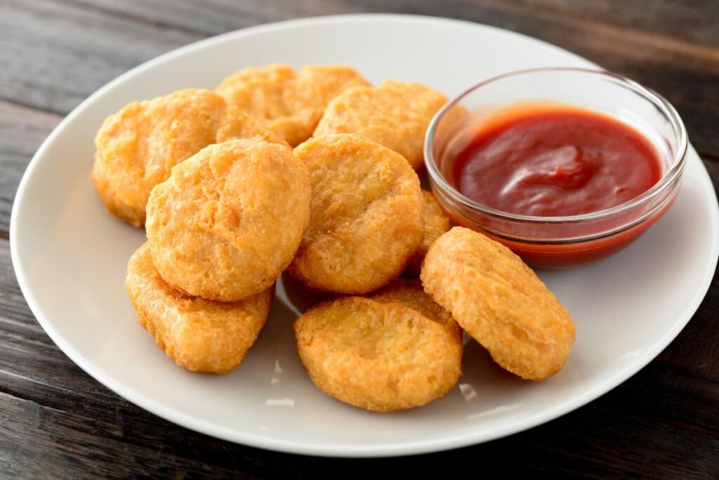 Chick Fil A Nuggets serves in a white plate, along with there is a red ketchup in a small glass bowl. 