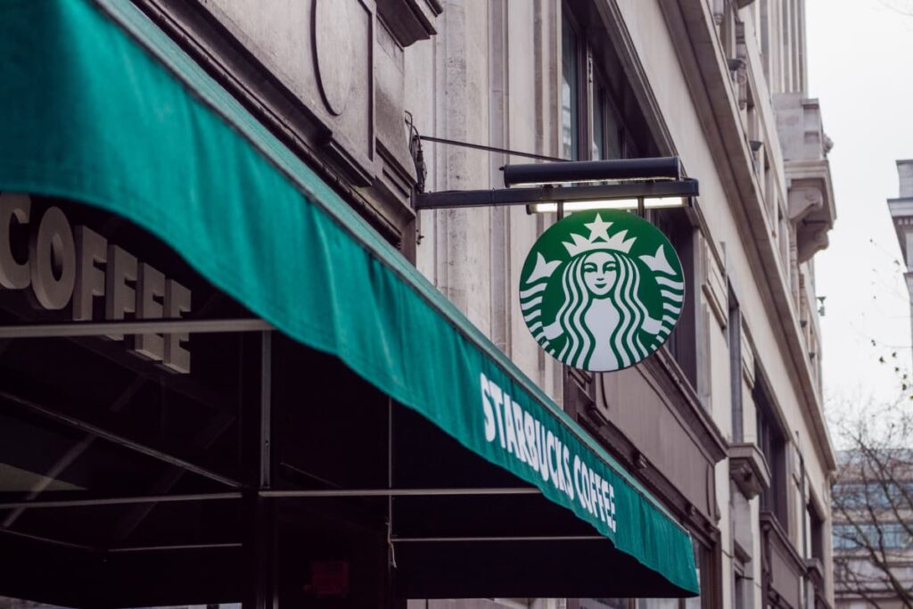 Starbucks have around 23,000 locations in the world. All locations have the Starbucks logo which is mermaid with the green and white color. In a building green color cloth infront of the building, and mentioned starbucks coffee in white color. 