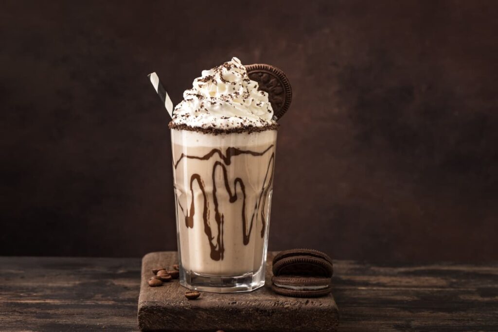 Starbucks Frappuccino Bottle has 320mg caffeine, and it is served in a Large glass. Starbucks frappuccino bottle is garnished with whipped cream, chocolate sauce, cream biscuit, choco powder and one straw. Beside the glass there are 2 cream biscuits and another side some beans.