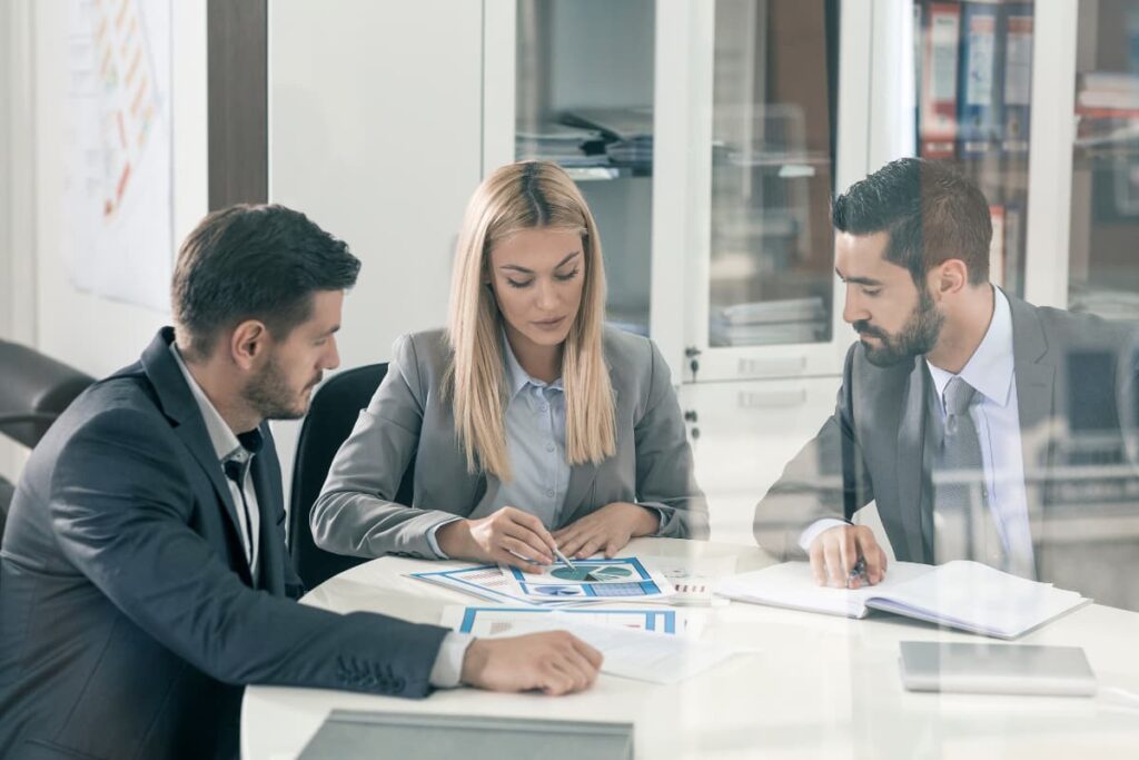 Chick Fil A Manager dicussing their projects with their team members. There are 3 members are sitting around the table, which are one female wears suit and besides of her 2 boys who wears suit.