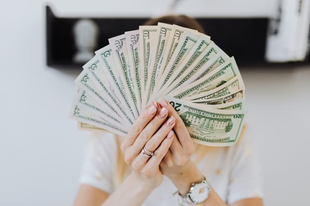 Starbucks Shift Supervisor can make money by hourly basis. Here a lady holding some dollars in her hands, she wears gold color ring, white color watch and white color t-shirt.