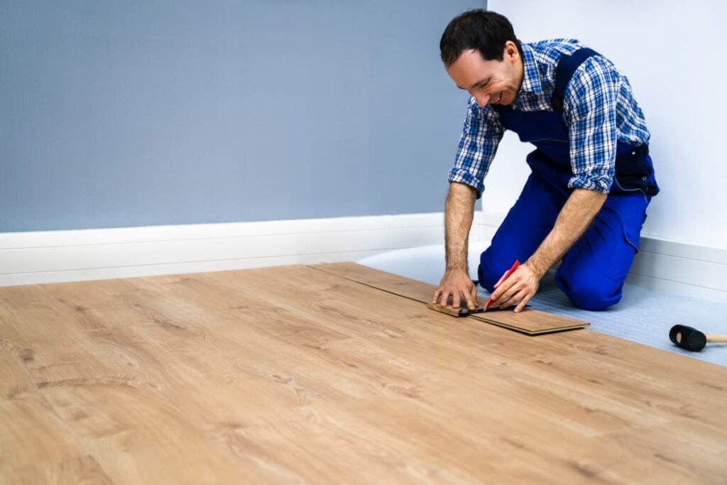 Lowe's Laminate Flooring was installing by an associate who has a red marker in his hand and measuring for installation.