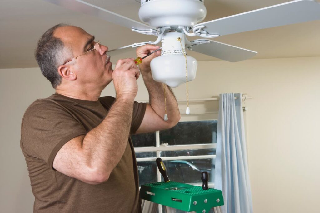 Lowe's Ceiling Fan is installing by an associate from Lowe's with a screw driver in his hand and a tool box beside him.