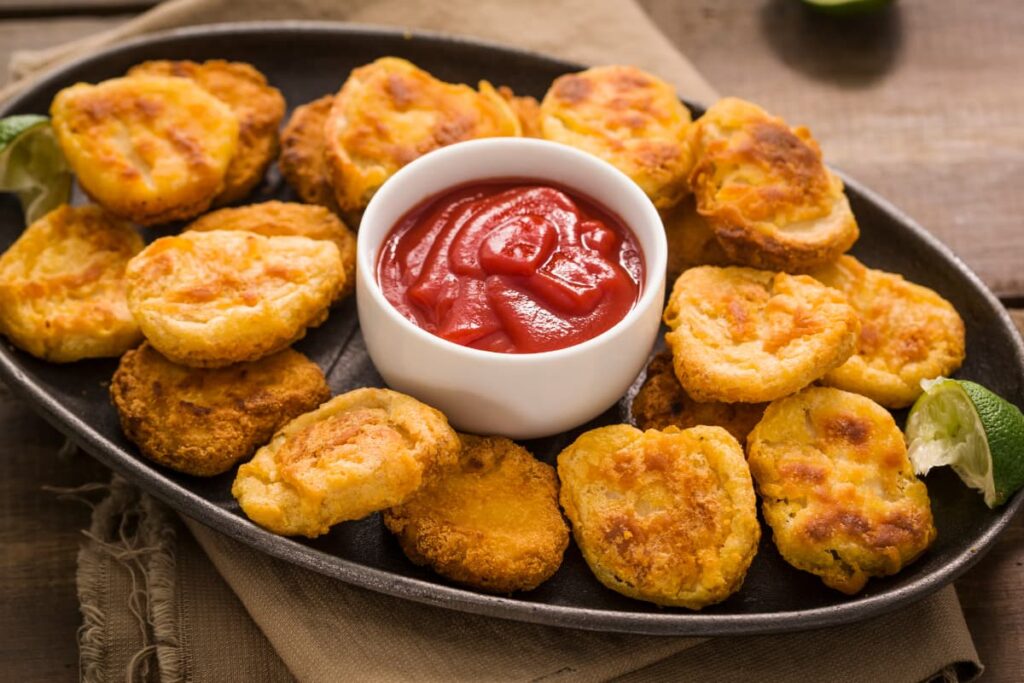 Chick Fil A Nugget Tray has around 20 nuggets along with 2 slices of lemon and red sauce ketchup in a small white bowl which is kept in the middle of nuggets.