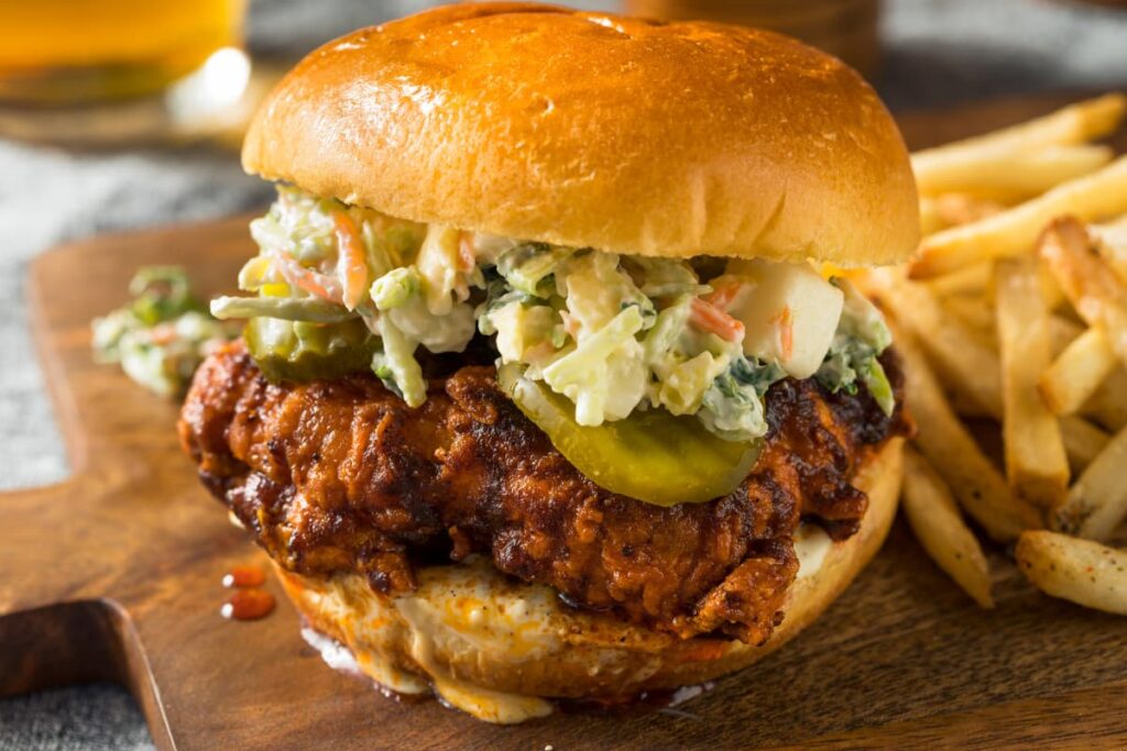 Chick Fil A Sandwich is served in a brown color wooden plate along with french fries. This chicken sandwich contains crispy chicken, one bun, jalapeno, cheese, and salad. 