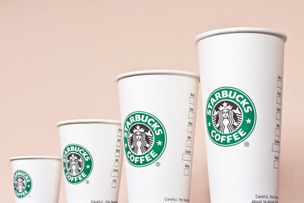 Starbucks Trenta is the large cup, which is last one from left to right. Each trenta has starbucks coffee logo at the middle of the cup, Which is green and white color.