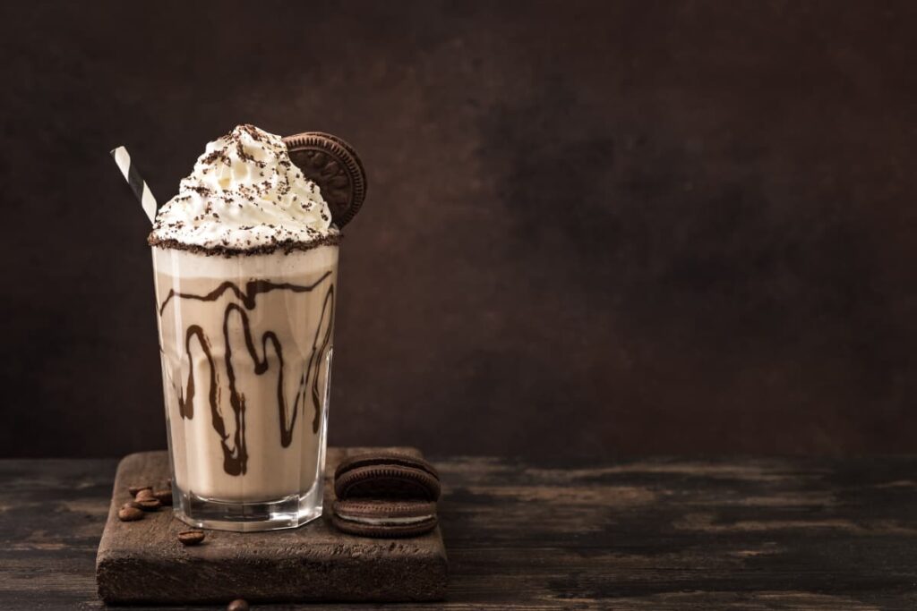 Starbucks Venti Frappuccino serves in a glass, and it is garnished with the whipped cream, choco powder, Chocolate sauce, one cream biscuit along with the straw. Beside the venti Frappuccino there are 2 biscuits and some choco beans on the base.