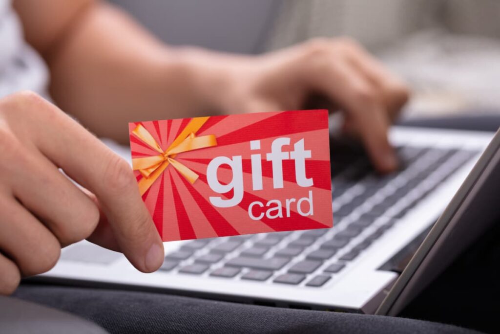 Burger King Gift Card is in red and white color combination card. A person is holding a Burger King Gift Card with his/her right hand, with another hand she/he typing in a keyboard.