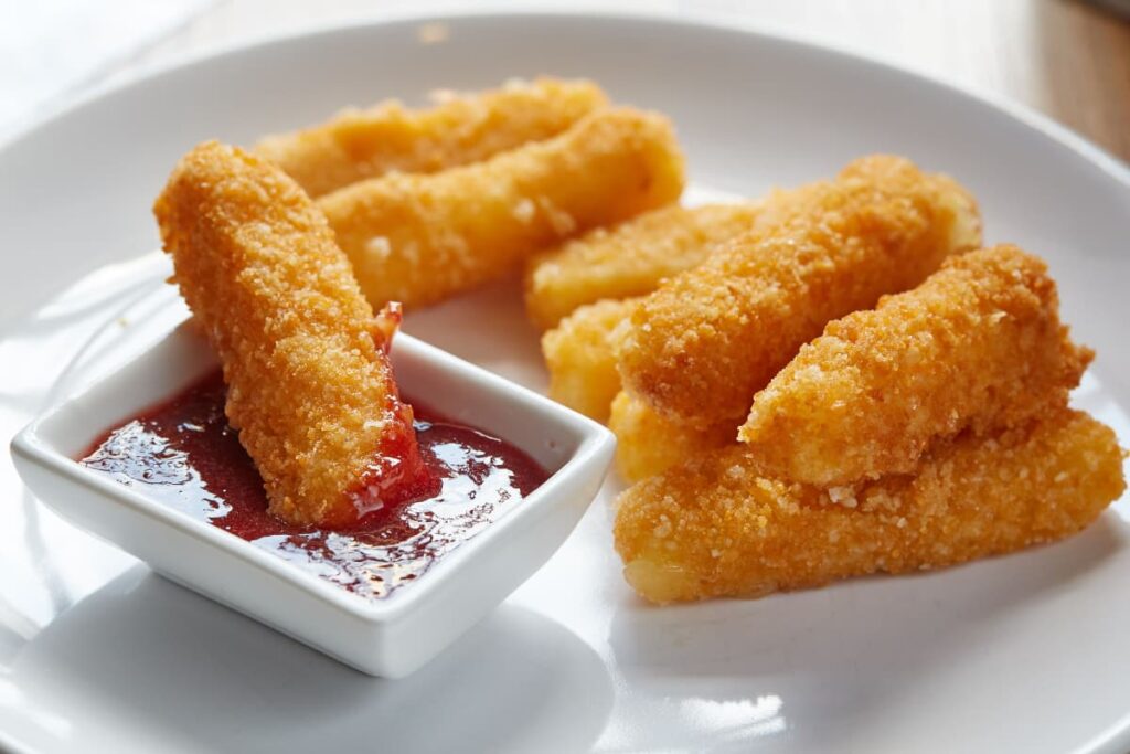 Chick Fil Grilled Nuggets are served in a white plate along with the ketchup which serves in a small white cup. Some grilled nuggets are placed in the bottle and one nugget is dipped in the red ketchup.