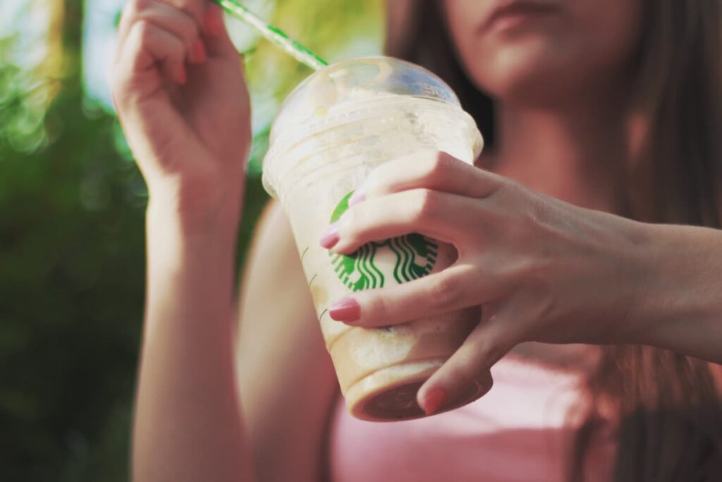 Starbucks Coffee can be served in a starbucks cup along with the straw. Here a girl who wears pink t-shirt holding a coffee cup with her left hand and a straw with her right hand. 
