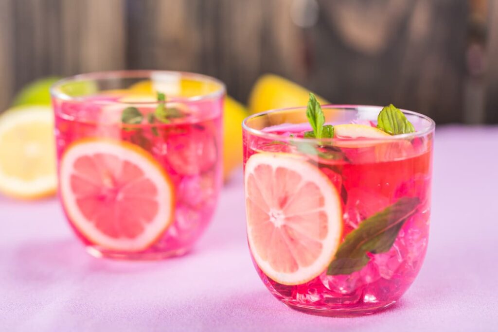 Starbucks Pink Drink serves in a Glass, pink drink looks like pink color and it is garnished with lemon slices and mint leaves. Beside the glasses there are sliced lemons on the floor.