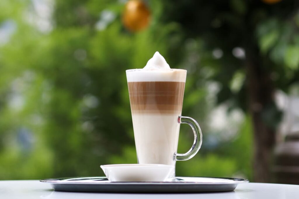 Starbucks Serve Its First Caffe Latte in a glass along with the saucer. This Caffe Latte is brown and white color, White milk on bottom of the glass, coffee on top and whipped cream on top of the coffee. 