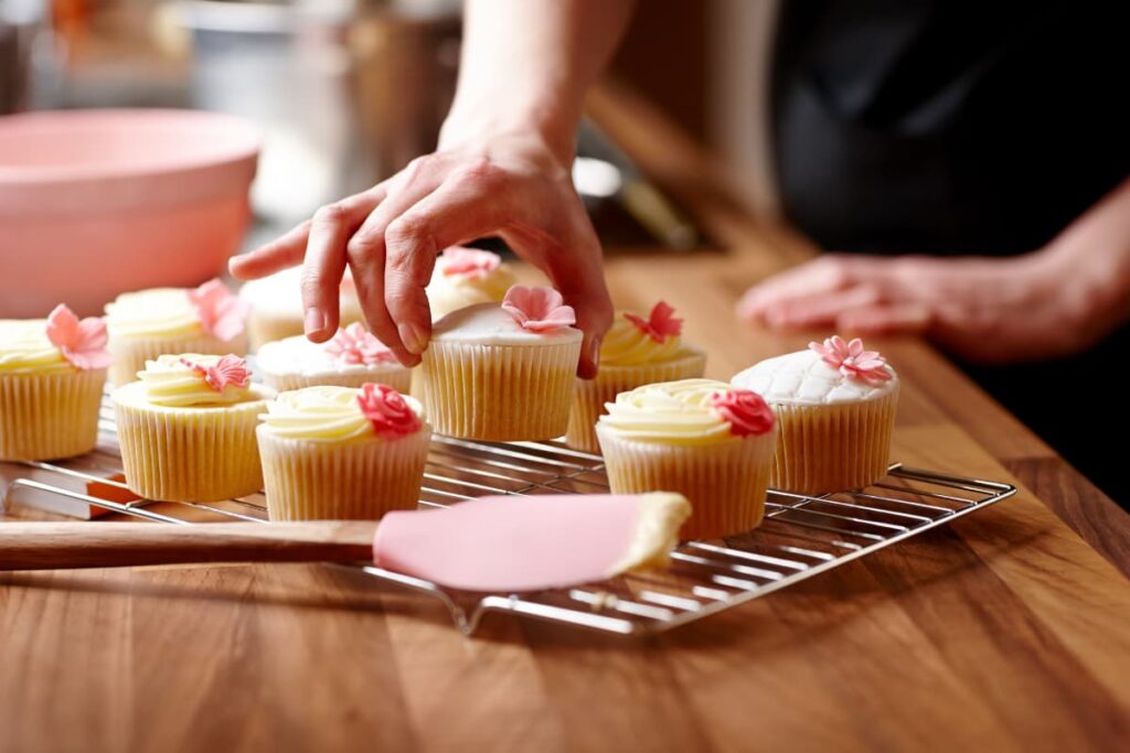 Walmart Baker arranged mini cupcakes with rose flower frosting on a steel grilled tray along with pink bowl and pink spatula.