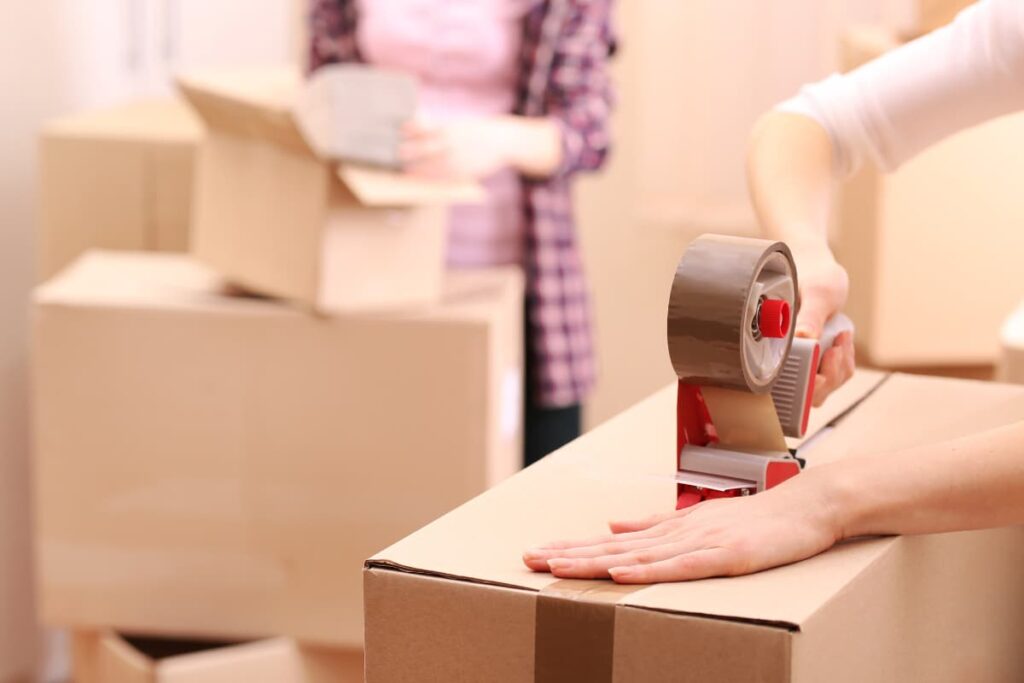 Two women packaging products using Walmart Boxes with the help of Tape Machine.