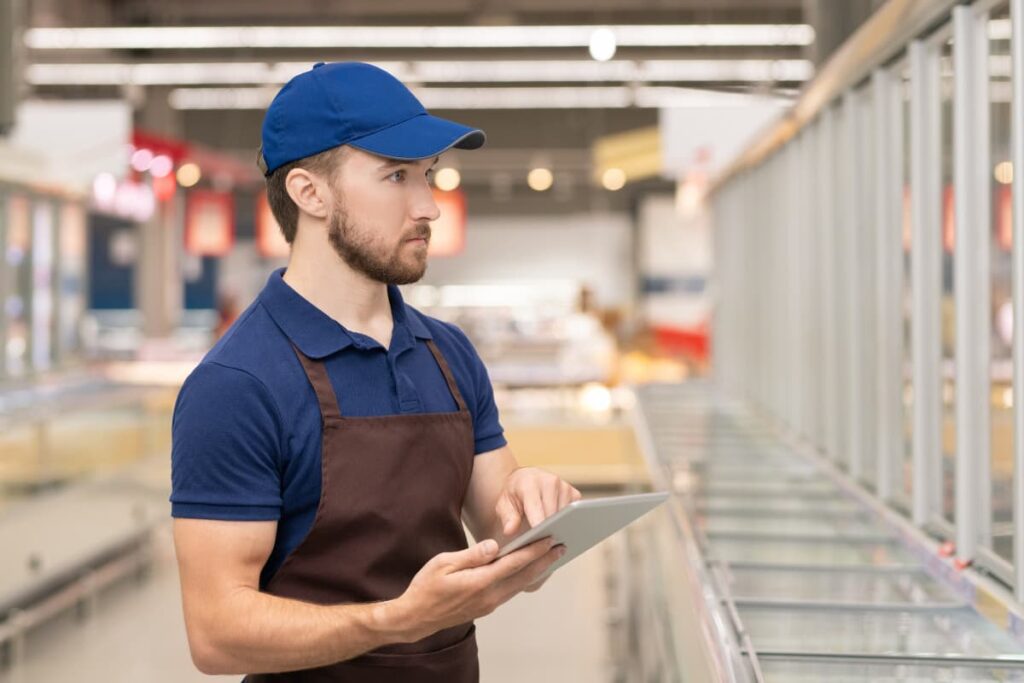 General Merchandise employee At Walmart Store to checking the stock at Inventory by using iPad and wearing blue color cap and uniform.