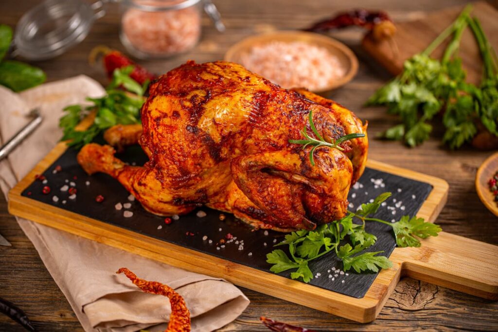 Walmart Rotisserie Chicken served in a wooden plater along with coriander leaves, dried chilies, brown sugar on a wooden table.
