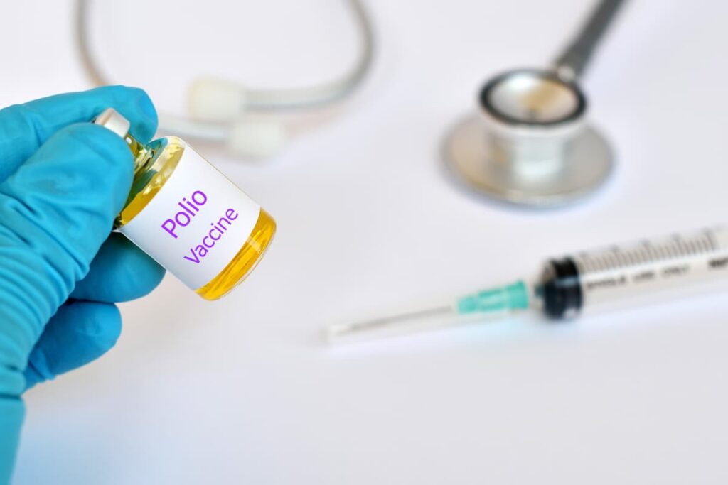 Walmart Vaccines are prescribed by  a doctor who is  holding polio Vaccine bottle with the help of plastic disposable syringe and wearing surgical gloves, Stethoscope.