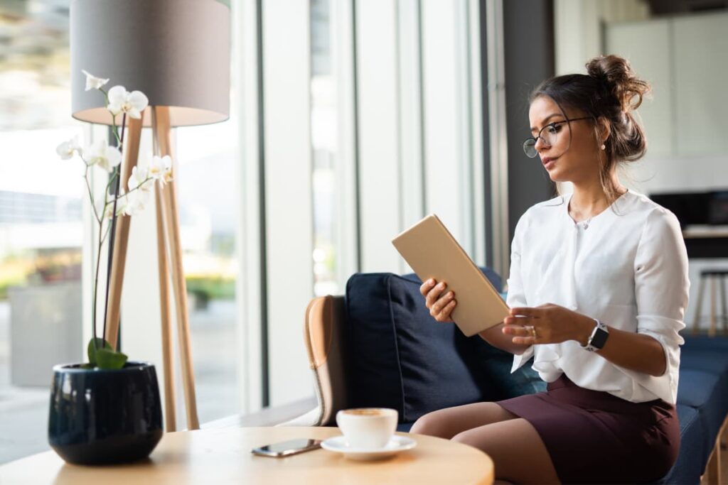 A women sitting in a couch watching Walmart ipad while having her Tea along side with her one table lamp light and a flower pot.  