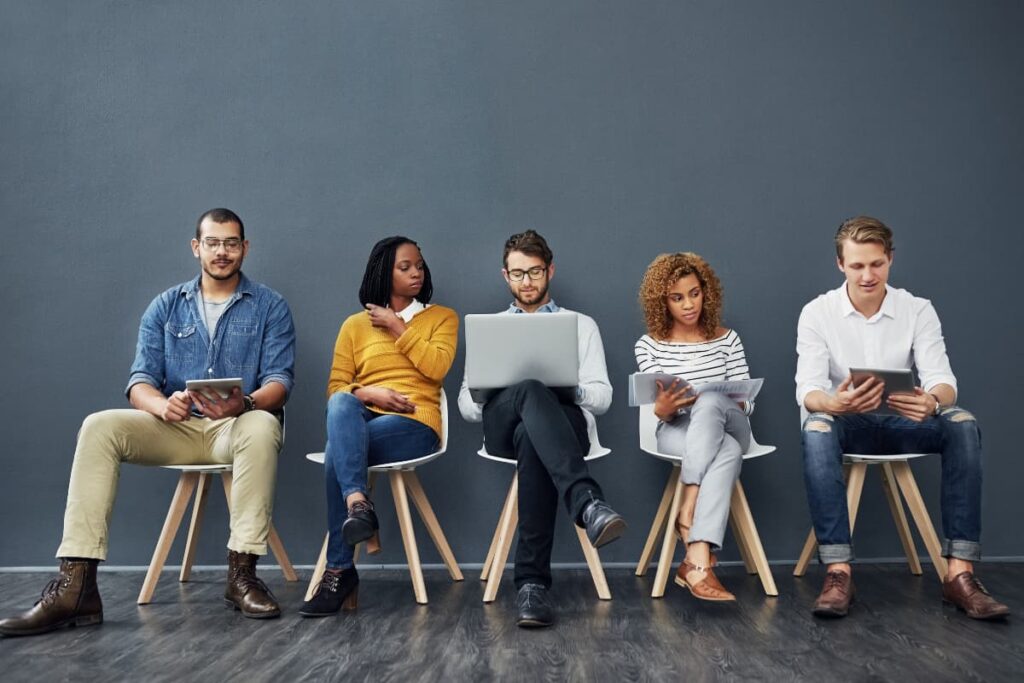 Chick Fil A Hires different age group of people. There are 5 people sitting on the 5 chairs wearing shoes and some hold laptops and some holds books.