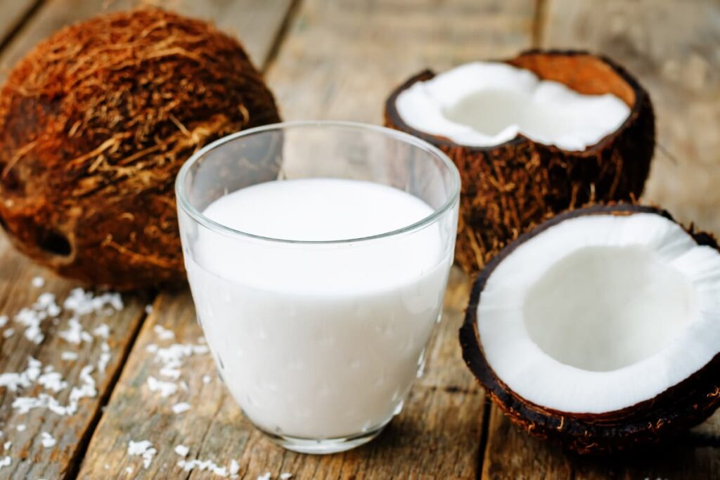 Starbucks Coconut Milk is in a glass, which is white in color. On a table there is a glass of coconut milk, 2 half coconut and one whole coconut.