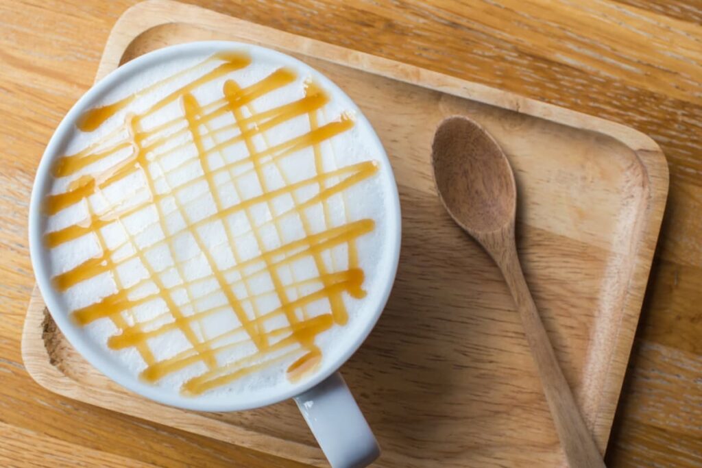Starbucks Macchiato serves in a white cup and it is garnished with the caramel on the white foam. Starbucks Macchiato serves in a wooden plate which is brown in color along with the wooden spoon.