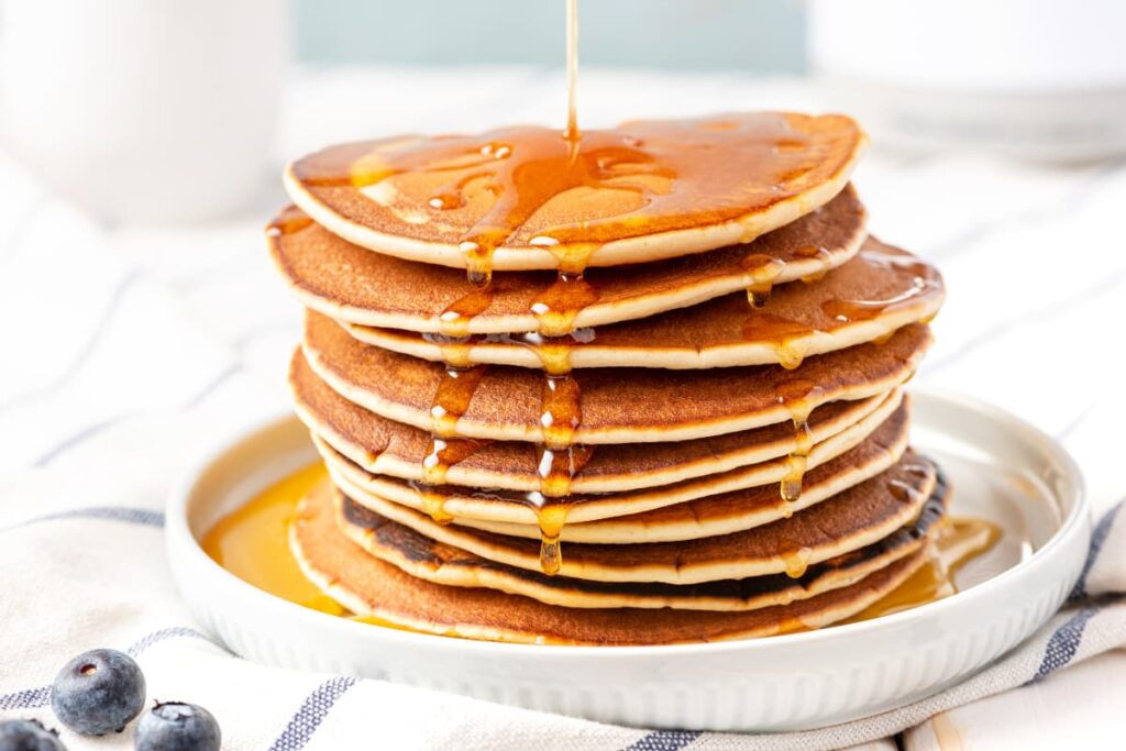 Starbucks Classis Syrup can be served with the combination of pan cakes. These pan cakes and starbucks classic syrup can be served in a white plate. Beside there are 3 blue berries on the floor.