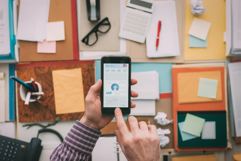 Walmart App downloaded by a person through Android Mobile on his office desk contains spectacles, pen, telephone, calculator, papers, pen holder and files.