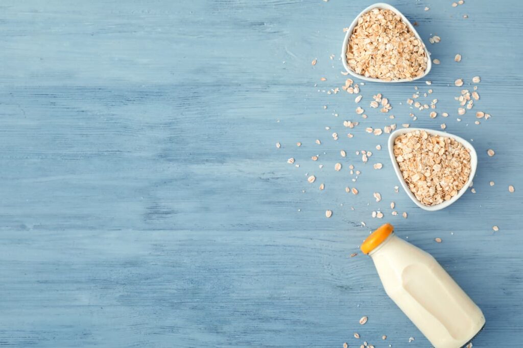 Starbucks Use Oatmilk, Oatmilk serves in a bottle with the yellow cap. On a table 2 white cups of oats are there, and some oats are on the ground.