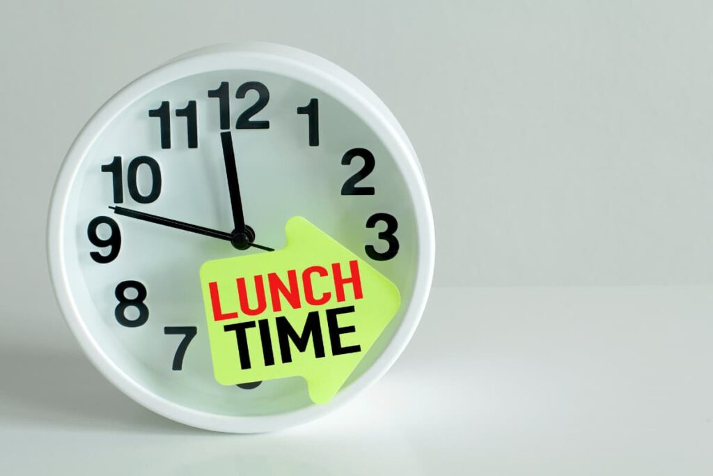 Chick Fil A Serve Lunch at Quarter to 12PM which shows on the White Clock placed in white table. On the clock it has Lunch time arrow and numbers from 1 to 12 which are black color.