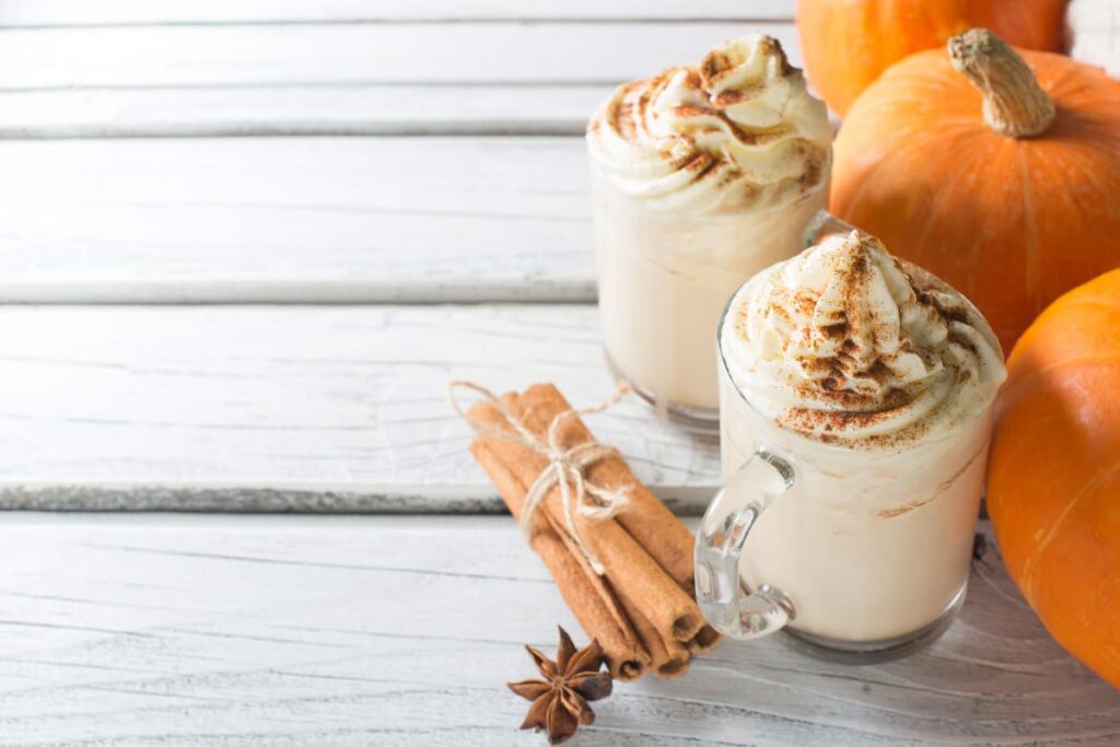 Pumpkin Spice Come Back To Starbucks, pumpkin spice is served in a 2 glass jars and those are garnished with cinnamon powder. Beside pumpkin spice glasses, there is a bunch of cinnamon, one star anise and 3 pumpkins, which is orange in color.
