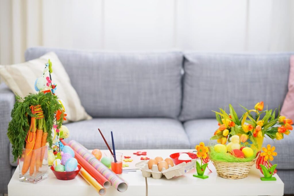 Walmart Easter Stuff contains Easter eggs , carrots, colorful sheets, paints, flower basket, artificial flowers on a table in front of couch.