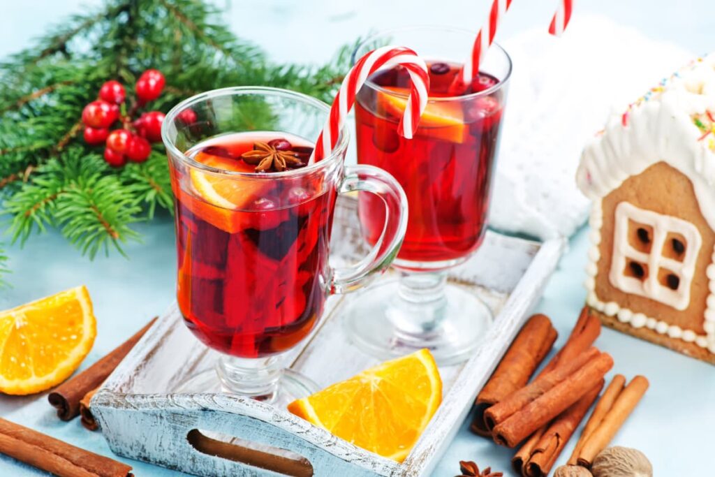 Starbucks Christmas Drinks are served on christmas day. Christmas drinks can be served in a glass jars, which is red in color and the drinks are garnished with star anise, lemon slices along with the straw. Beside there are some lemon slices, cinnamon sticks, christmas leaves, red cherries and a small toy house.