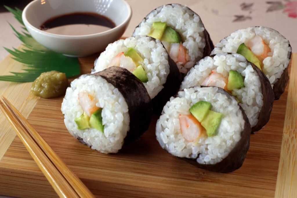 Sushi at Safeway served with sauce , chop sticks on a wooden serving tray.