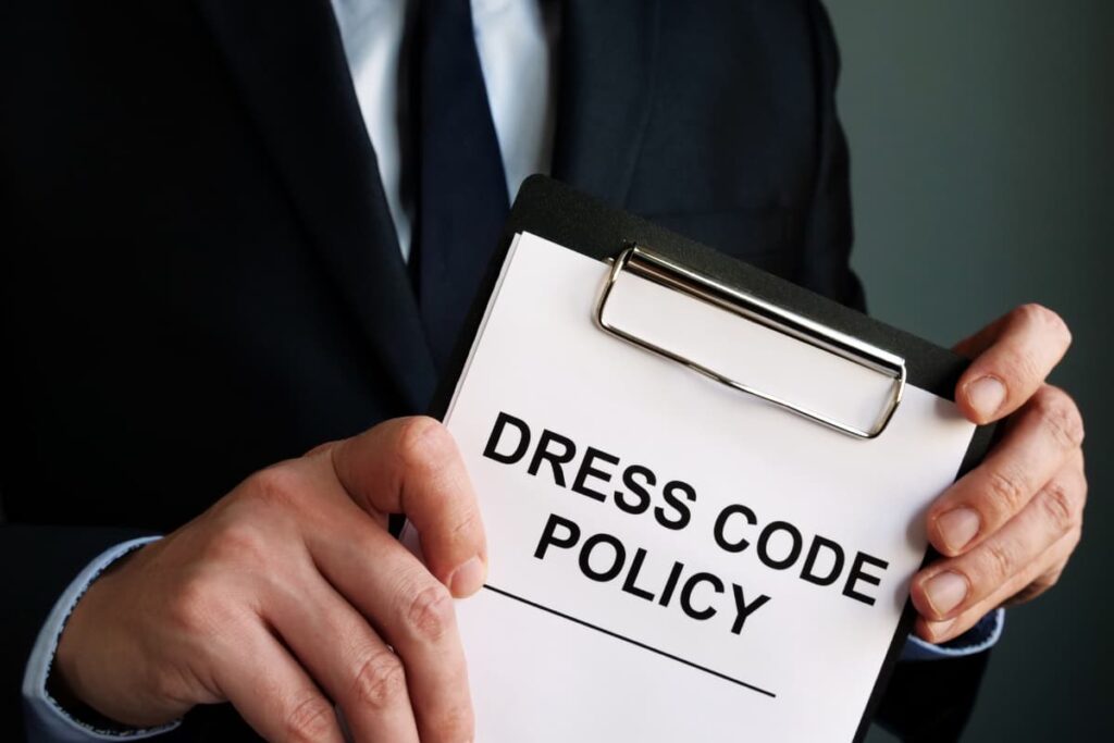 Starbucks Have A Dress Code, A man holding dress code policy board which is written black in color on the white paper. The person who holds the board wears blue color suit and white color shirt.