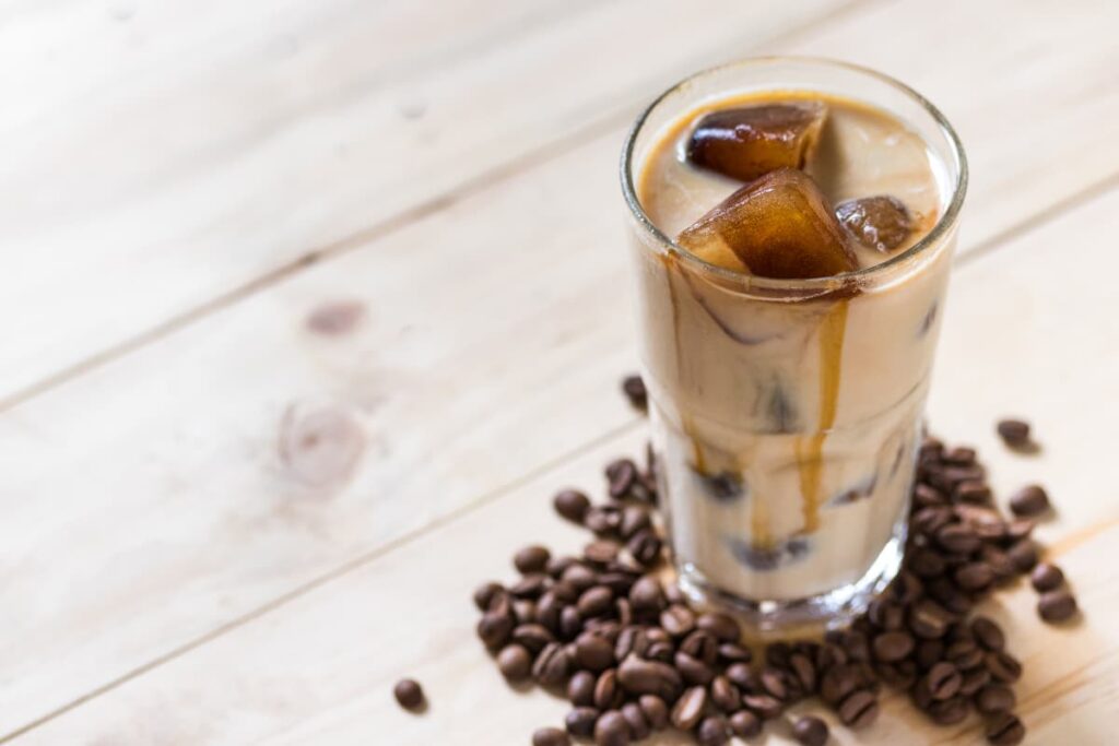 Starbucks Venti Iced Coffee can be served in a glass, and it is garnished with ice cubes and syrup. Starbucks Venti Iced Coffee looks liteblue color and coffee beans are surrounded by the glass.