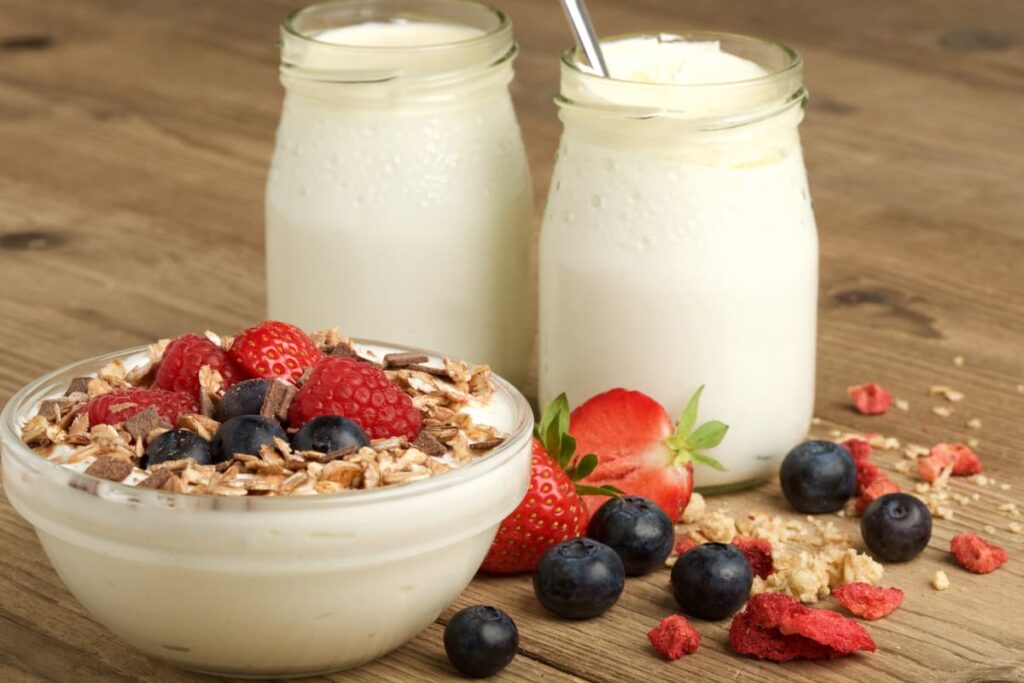 Starbucks Yogurt can be served in a glass cup, and it is garnished with strawberries, blue berries and roasted oats. Beside there are 2 glasses of yogurt and half cut strawberry, some blueberry and some oats are sprinkled on the floor.